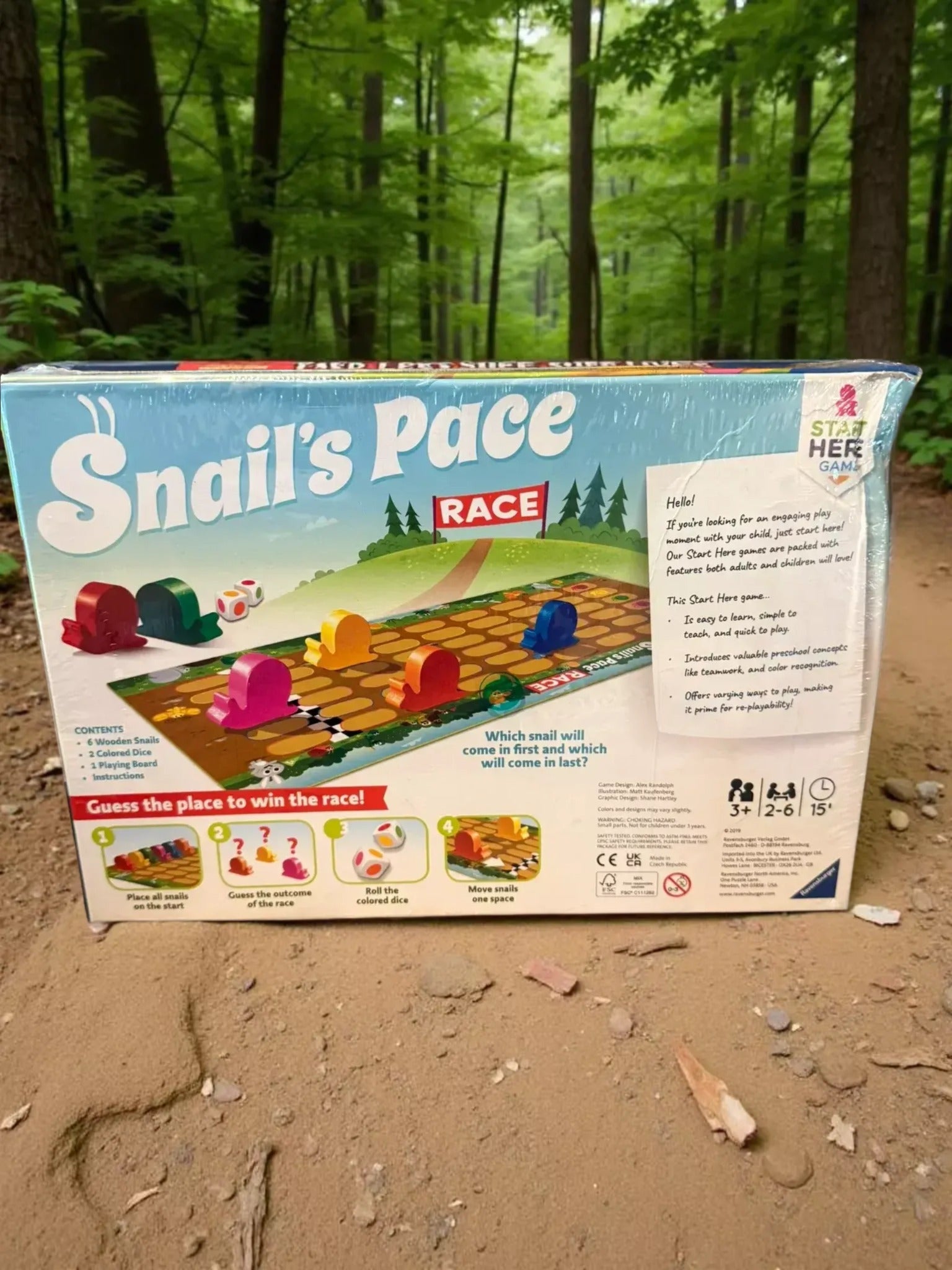 a Snail's Pace game box placed on a dirt ground, with a forest in the background.