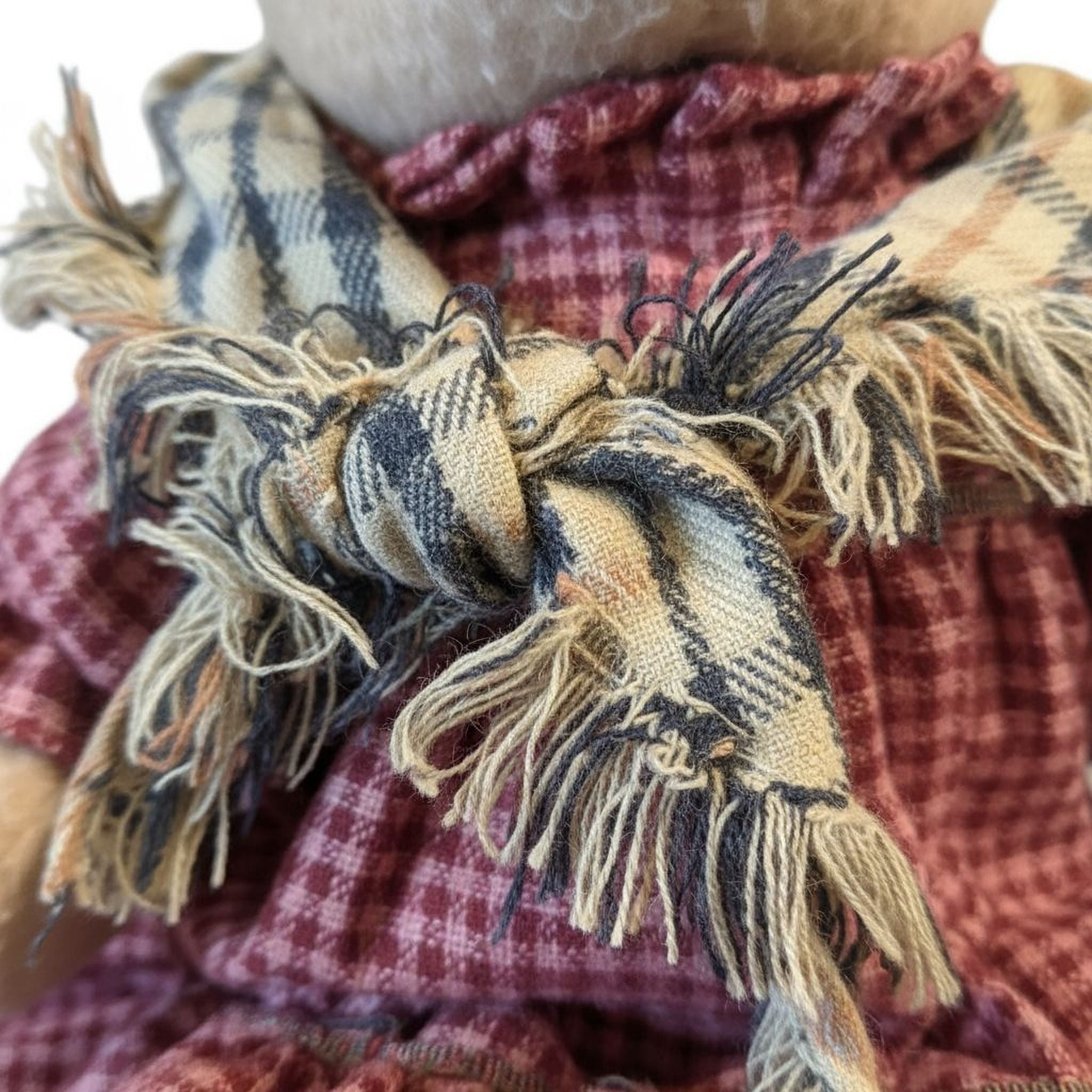 A close-up image of a teddy bear wearing a plaid scarf with fringed edges.