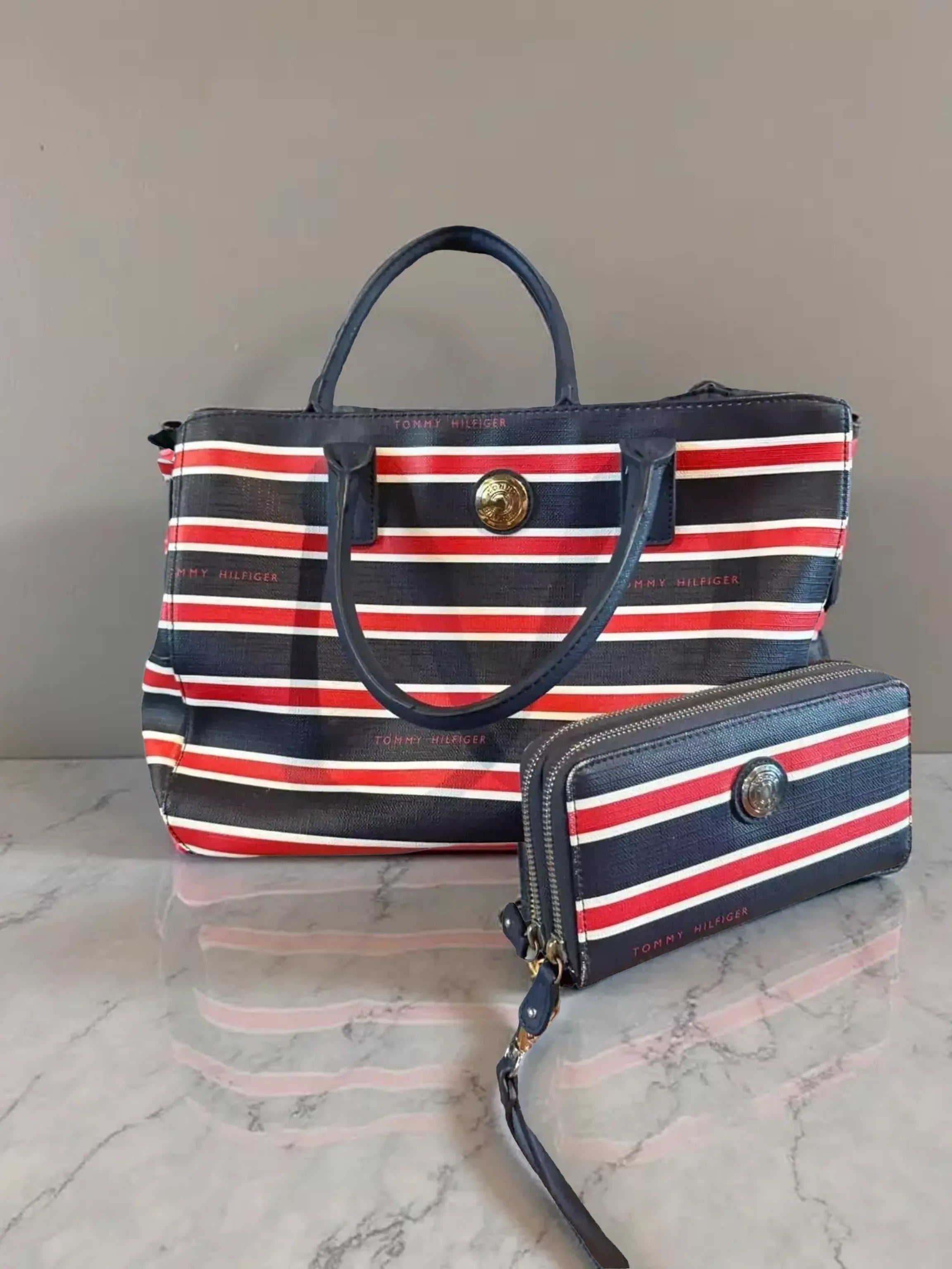A striped handbag and a matching wallet are displayed on a stone surface, with a brick wall in the background.