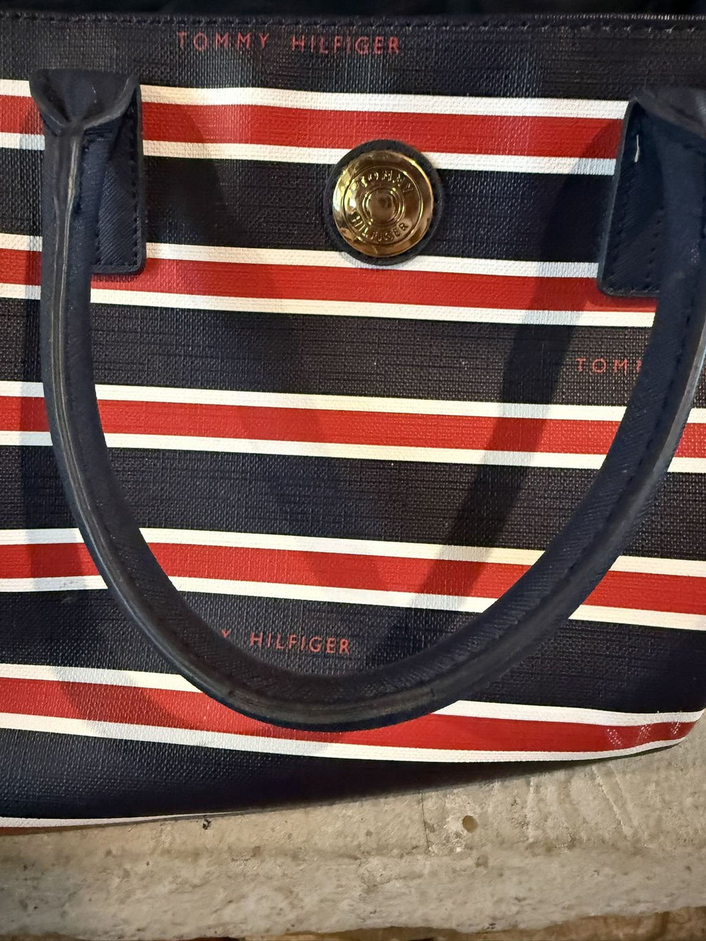 A close-up image of a striped handbag with a gold-colored logo on the front.