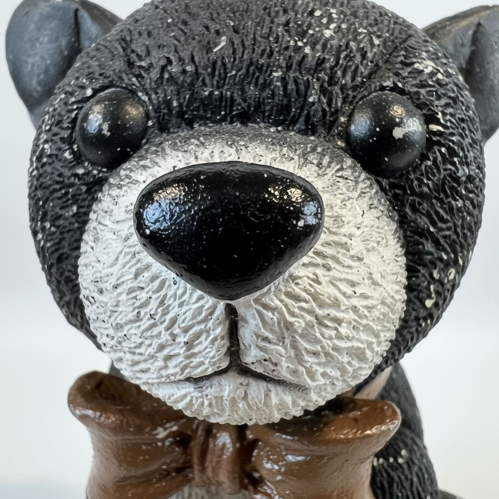 A close-up image of a black and white teddy bear with a brown bowtie.