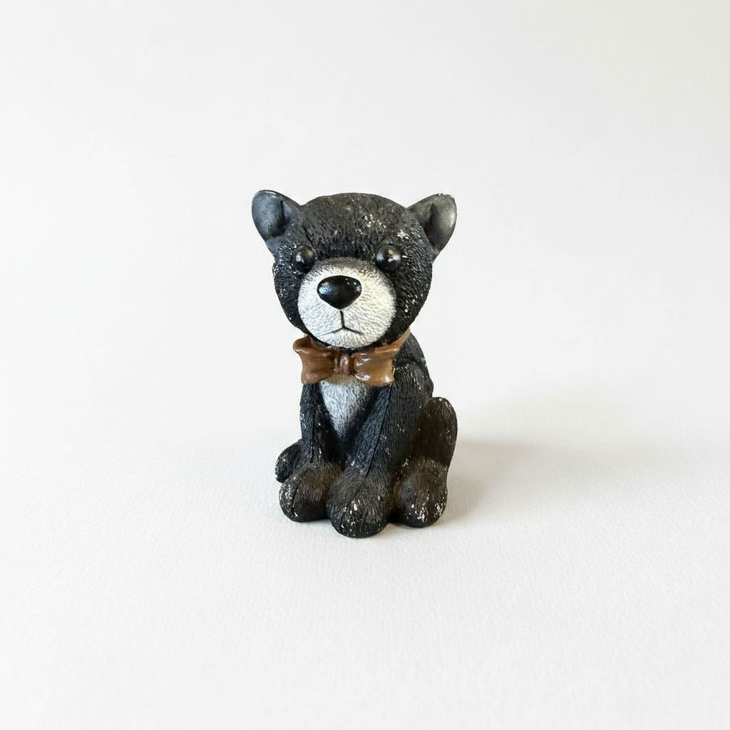 A small, black and white stuffed animal figurine wearing a brown bow tie sits on a plain white background.