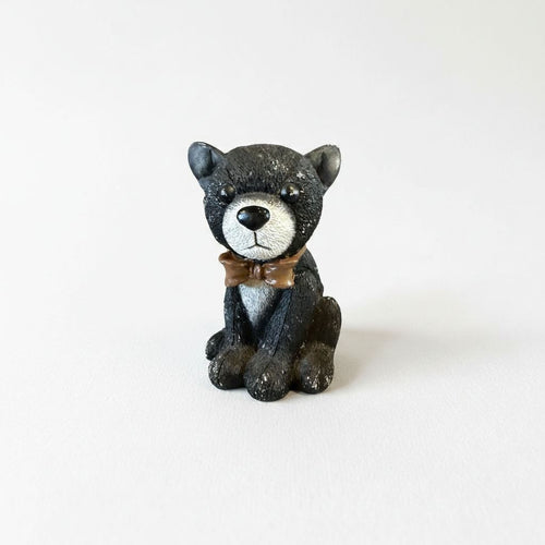 A small, black and white stuffed animal figurine wearing a brown bow tie sits on a plain white background.