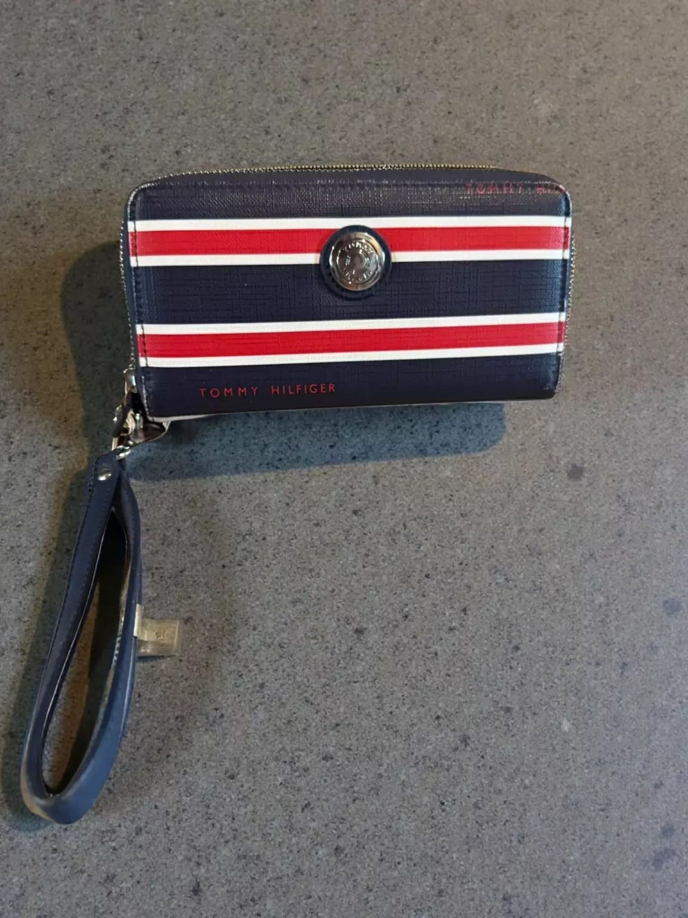 A navy blue and red striped wallet with a metallic emblem on the front, placed on a stone surface.
